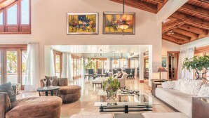 A spacious living area with a modern design, featuring a large sofa, a coffee table, and a dining area. There are two paintings on the wall and a ceiling with wooden beams. - Wonderful Villa w Style at Colinas Casa de Campo (La Romana)