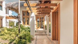 Een modern gebouw met een houten pergola, rieten dak en een betonnen pad dat naar een houten deur leidt.