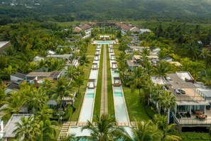 Vista aérea de un resort con una piscina central, rodeado de villas y palmeras.