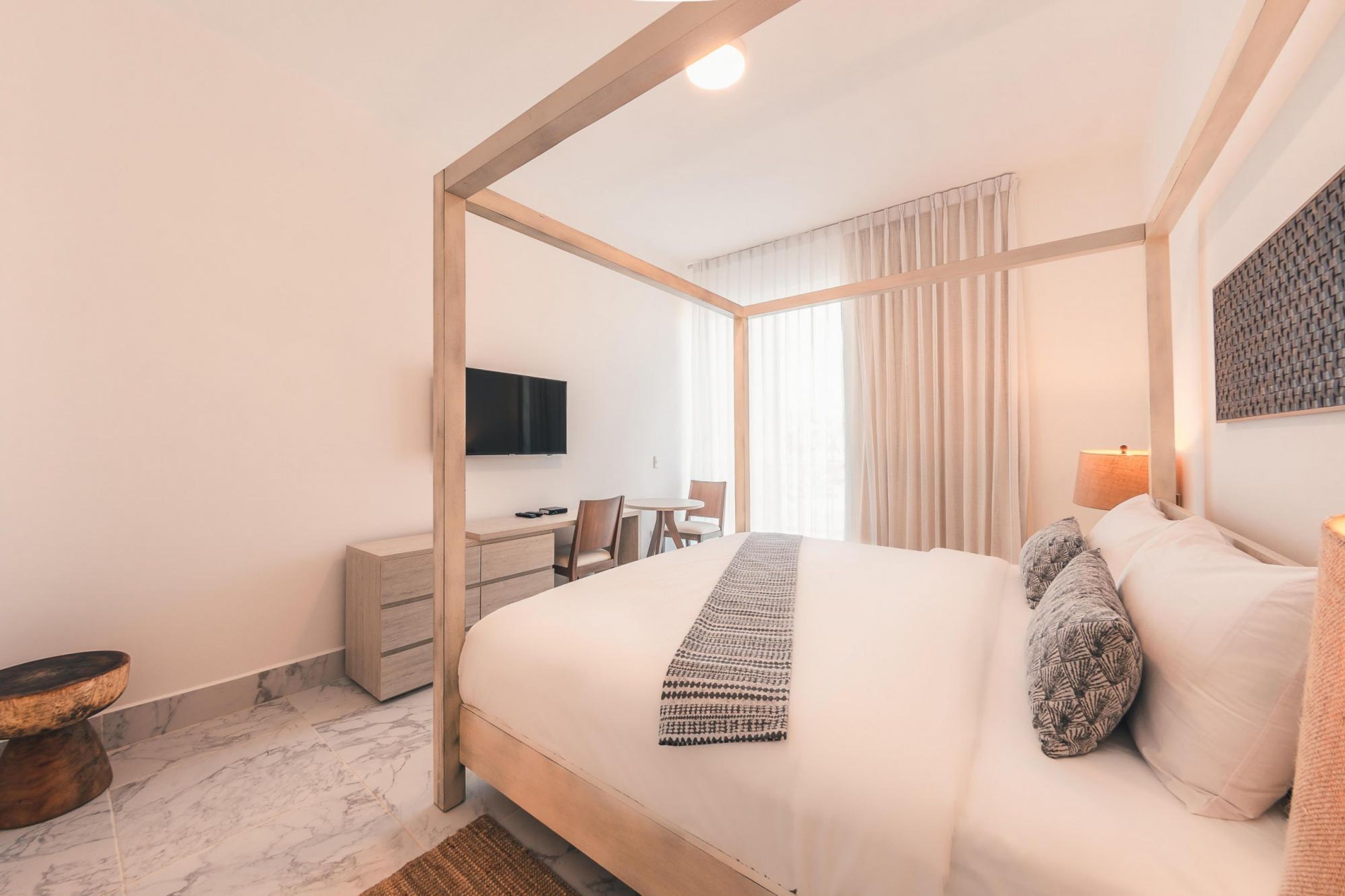 Quarto de hotel moderno com uma cama grande, uma escrivaninha, uma cadeira e uma televisão.