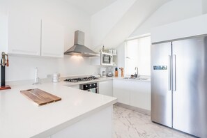 A modern kitchen with white cabinetry, a stainless steel refrigerator, a gas stove, and a marble floor. - 3br-penthouse w Jacuzzi Incl at Lake View (Las Terrenas)