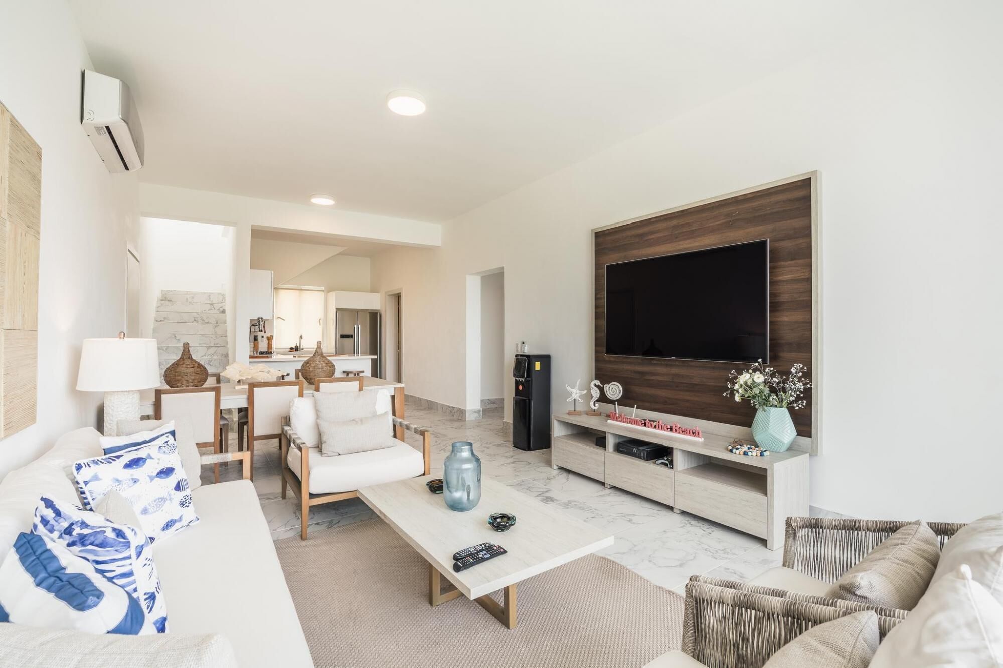 Una sala de estar moderna con un televisor grande, una zona de comedor y una cocina al fondo.