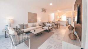 A modern living room with a sofa, chairs, a coffee table, and a kitchen in the background. - 3br-penthouse w Jacuzzi Incl at Lake View (Las Terrenas)