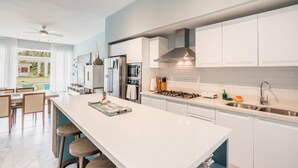 A modern kitchen with white cabinetry, a central island with stools, a gas stove, and a view of a pool outside. - Two-bedroom apt With Pool View bbq in Lake View (Las Terrenas)