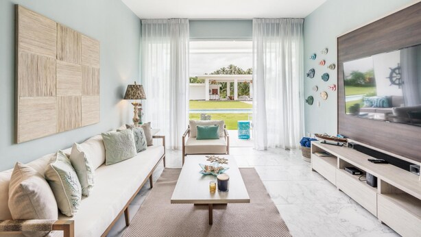 A modern living room with a sofa, coffee table, TV, and a view of a garden. - Two-bedroom apt With Pool View bbq in Lake View (Las Terrenas)