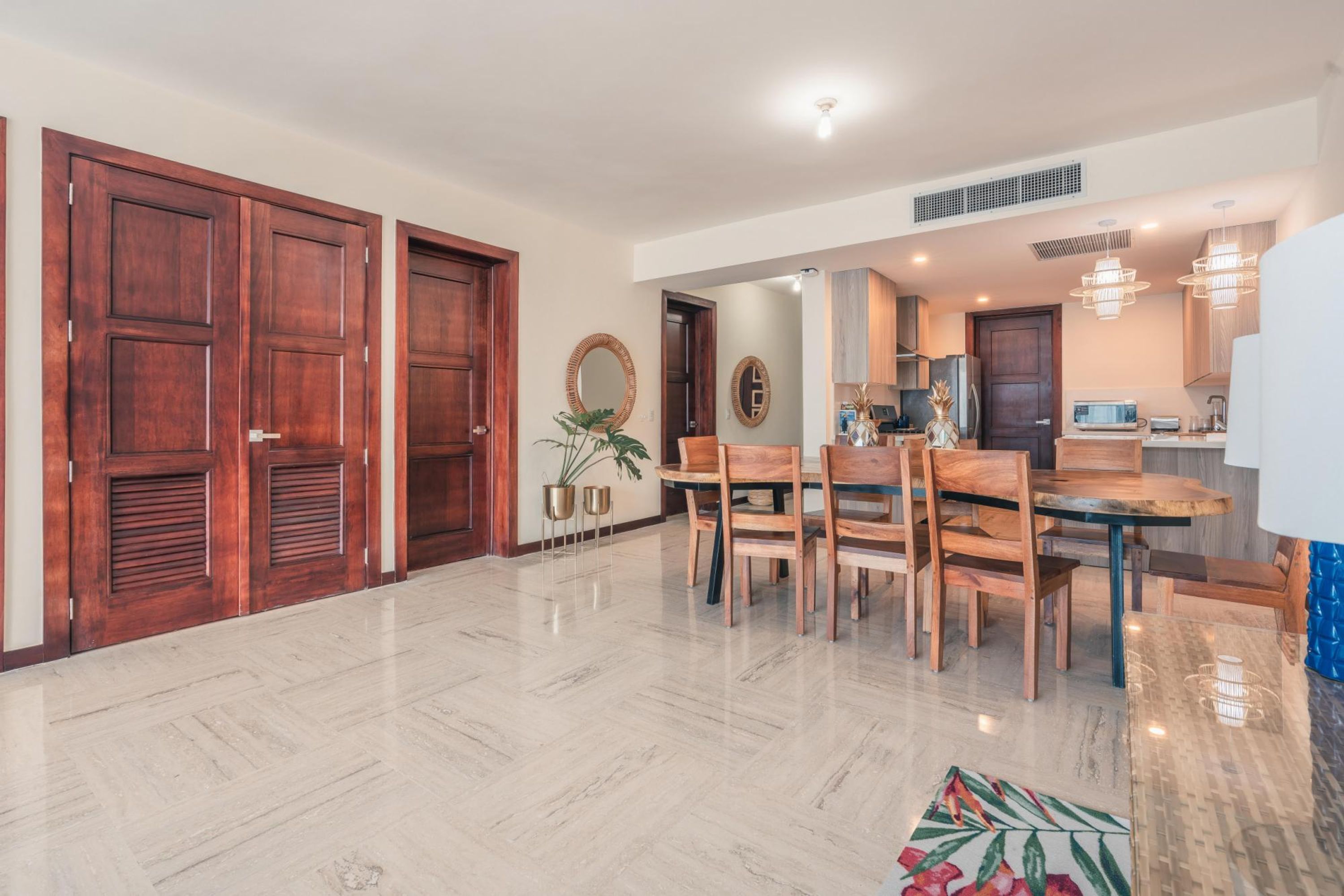 A spacious dining area with a wooden table and chairs, a large mirror, and a potted plant.