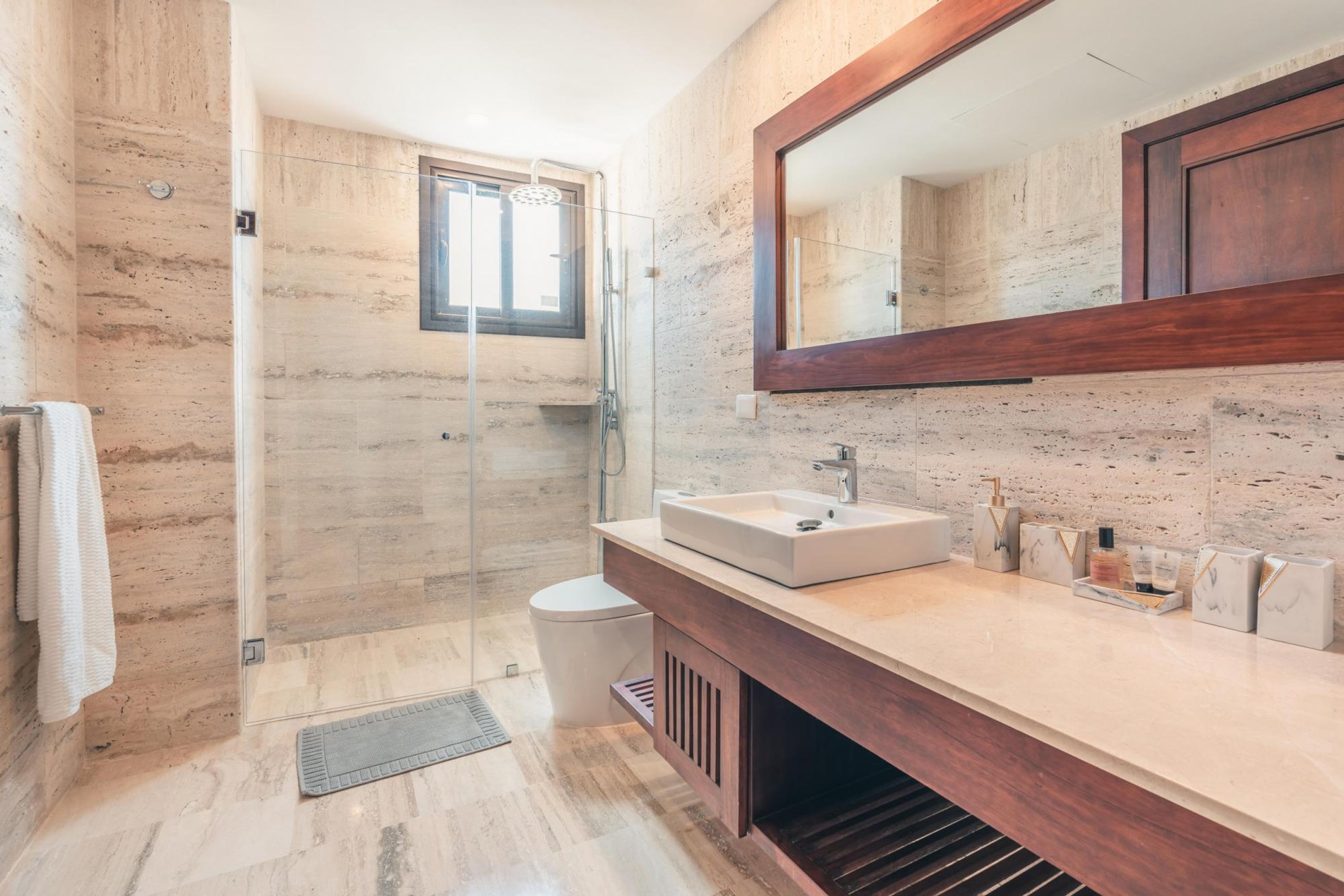 A modern bathroom with a glass shower enclosure, a large mirror, and a marble-tiled floor.