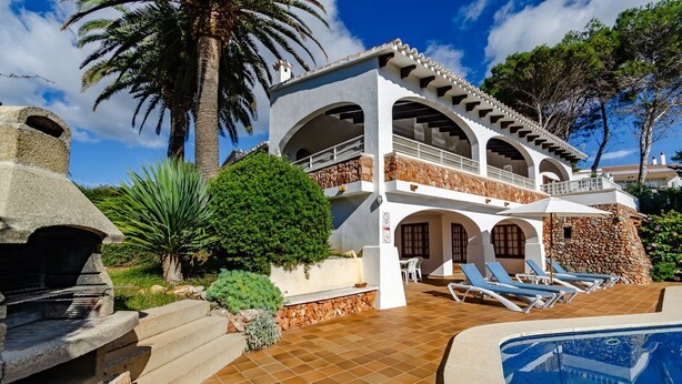 Ein zweistöckiges Haus mit Steinaußenwand, einem Swimmingpool und einer Terrasse mit Liegestühlen.
