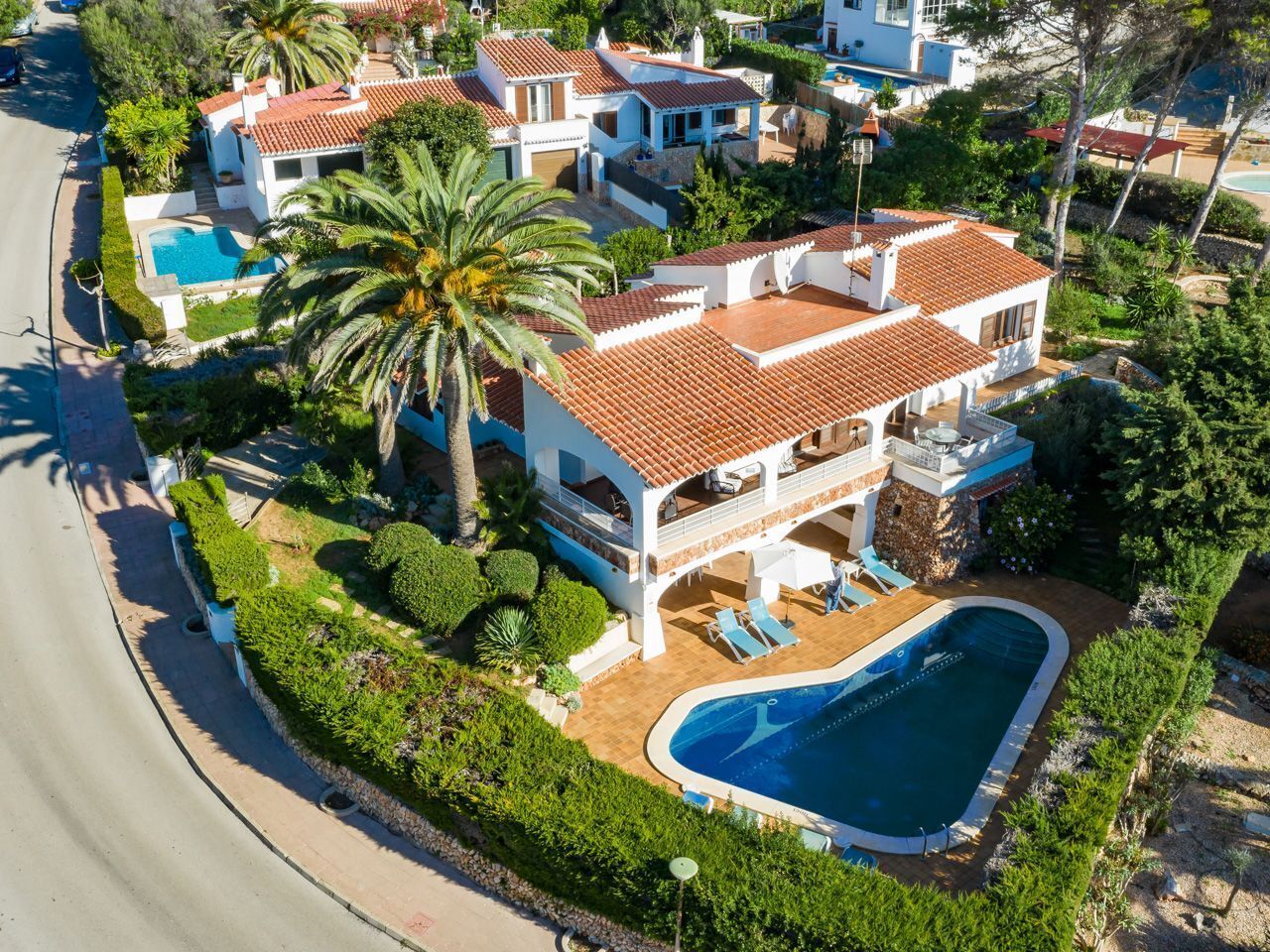 Ein großes, zweistöckiges Haus mit Swimmingpool, umgeben von üppiger Vegetation und Palmen.