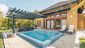 A swimming pool with a tiled edge, a pergola, outdoor seating, and a house with a tiled roof and large windows. - Tropical Villa With Pool at Green Village B843 (Punta Cana)