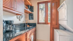 A compact kitchen with wooden cabinets, a black countertop, a coffee maker, a sink, and a window with a view of greenery. - Tropical Villa With Pool at Green Village B843 (Punta Cana)