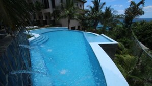 A swimming pool with a curved edge, surrounded by palm trees and a building in the background. - Pool Balcony Oceanview King Parking Full Kitchen - Flamingo Towers 25 (Cabo Velas)