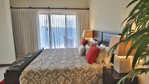 A bedroom with a large bed, a nightstand, a lamp, and a plant. - Pool Balcony Oceanview King Parking Full Kitchen - Flamingo Towers 25 (Cabo Velas)