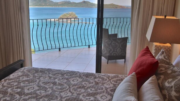 A hotel room with a bed, a chair, and a view of the sea through a balcony. - Pool Balcony Oceanview King Parking Full Kitchen - Flamingo Towers 25 (Cabo Velas)