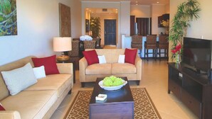 A living room with two sofas, a coffee table, a TV, and a dining area in the background. - Pool Balcony Oceanview King Parking Full Kitchen - Flamingo Towers 25 (Cabo Velas)
