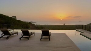 Une vue sur le coucher de soleil depuis un espace aménagé près de la piscine, avec des chaises longues et un horizon dégagé.