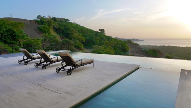 Une piscine à débordement avec des chaises longues et une vue sur l’océan.