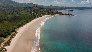 An aerial view of a coastal area with a sandy beach, clear blue waters, and a mountainous backdrop. - Flamingo Rose Vista in Playa Flamingo (Cabo Velas)