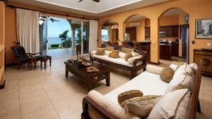 A spacious living room with a sofa set, a coffee table, and a chair. There is a view of the ocean through large windows. - Beachfront Potrero Nice 7-br Villa Chef Included - Casa Royal (Tempate)