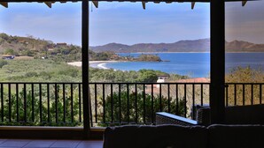 A balcony with a view of a coastal landscape, including a beach and distant hills.