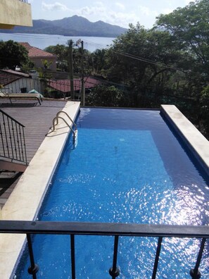 Piscina rectangular con barandilla metálica, rodeada por un solado de concreto y vista a un paisaje montañoso.