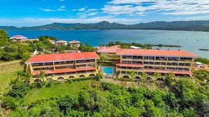 A resort with multiple buildings, a swimming pool, and a view of the sea and mountains.