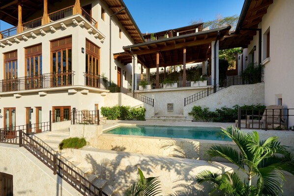 A two-story building with a swimming pool, outdoor seating, and a covered patio area.