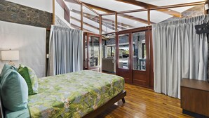 Une chambre à coucher avec un lit, des rideaux, un plancher en bois et une vue sur l’extérieur.