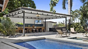 Un espace aménagé au bord de la piscine, avec un barbecue couvert et des sièges.