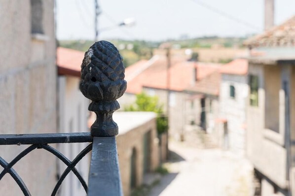 A metal railing with a decorative finial, overlooking a narrow street with buildings and a clear sky.