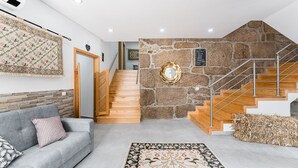A modern interior with a grey sofa, a patterned rug, and a stone wall. - Sevenfarm (Mangualde)