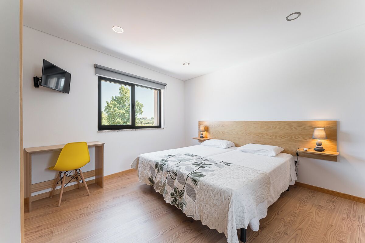 Quarto com cama, luminárias de cabeceira, escrivaninha e uma cadeira.