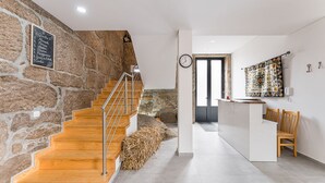 A modern interior with a stone wall, wooden staircase, and a reception area with a clock and decorative tiles. - Sevenfarm (Mangualde)