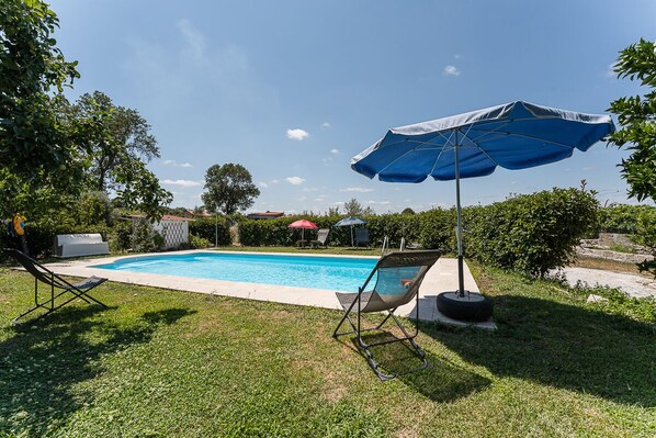 Una piscina con una sombrilla azul, una silla de jardín y un columpio hecho con un neumático.