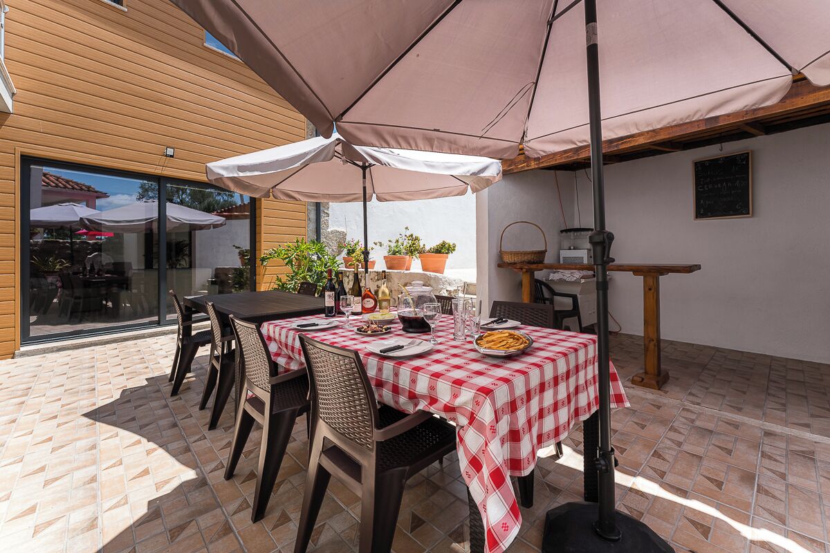 An outdoor patio with a table set for dining, surrounded by chairs and covered by a large umbrella.