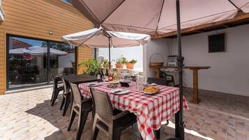 An outdoor patio with a table set for dining, surrounded by chairs and covered by a large umbrella.