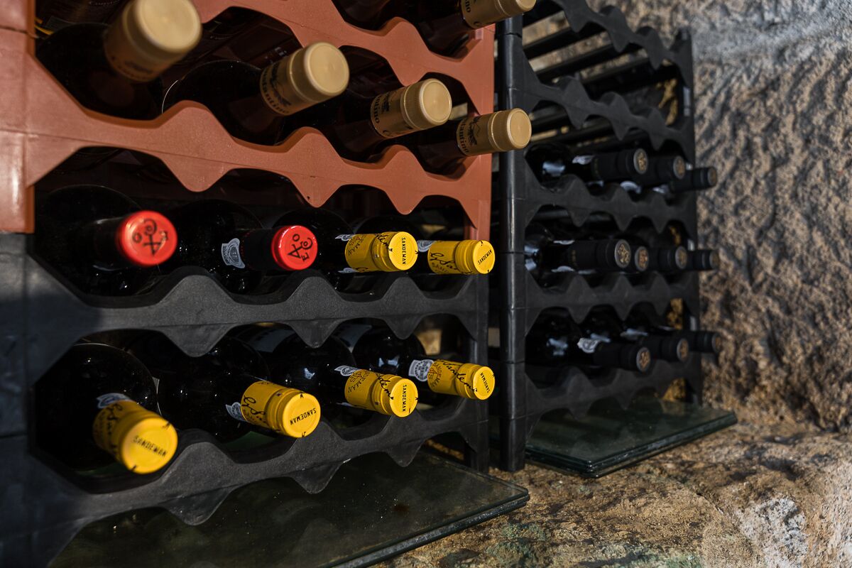 A wine rack with multiple bottles, some with yellow and red caps, against a textured wall.