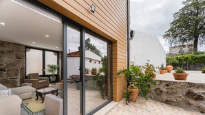 A modern house with a stone wall, wooden exterior, and a patio area with furniture and potted plants. - Sevenfarm (Mangualde)