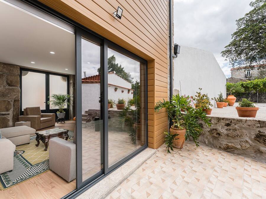 A modern house with a stone wall, wooden exterior, and a patio area with furniture and potted plants.