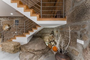 Una escalera moderna con escalones de madera y barandillas metálicas, que conduce a una zona superior con un muro de piedra y decoración rústica.