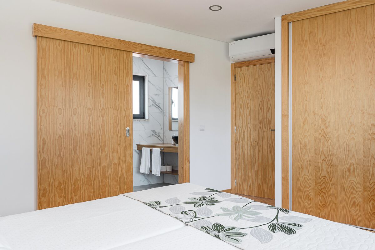 Une chambre à coucher avec un lit, une armoire en bois et une salle de bain visible à travers une porte ouverte.