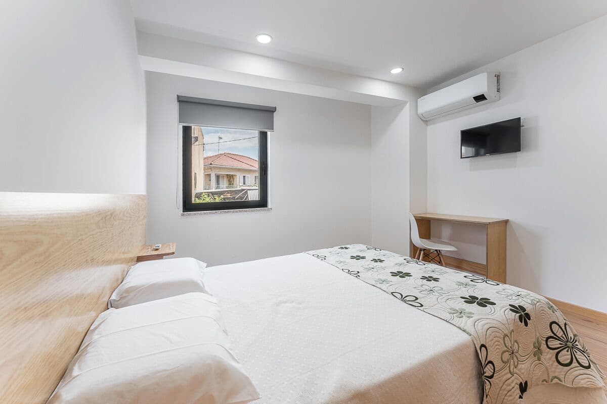 Une chambre à coucher comprenant un lit, un bureau, une chaise, une fenêtre et un appareil de climatisation.