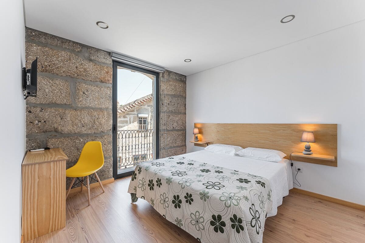Une chambre à coucher avec un lit, un bureau, une chaise et un mur en pierre.