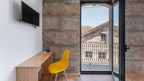 A room with a stone wall, a wooden bench, a yellow chair, and a TV mounted on the wall. - Sevenfarm (Mangualde)