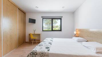 A bedroom with a bed, a desk, a chair, a TV, and a window.