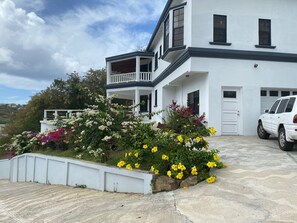 Una casa bianca a due piani con un balcone, un garage e un giardino ricco di fiori.