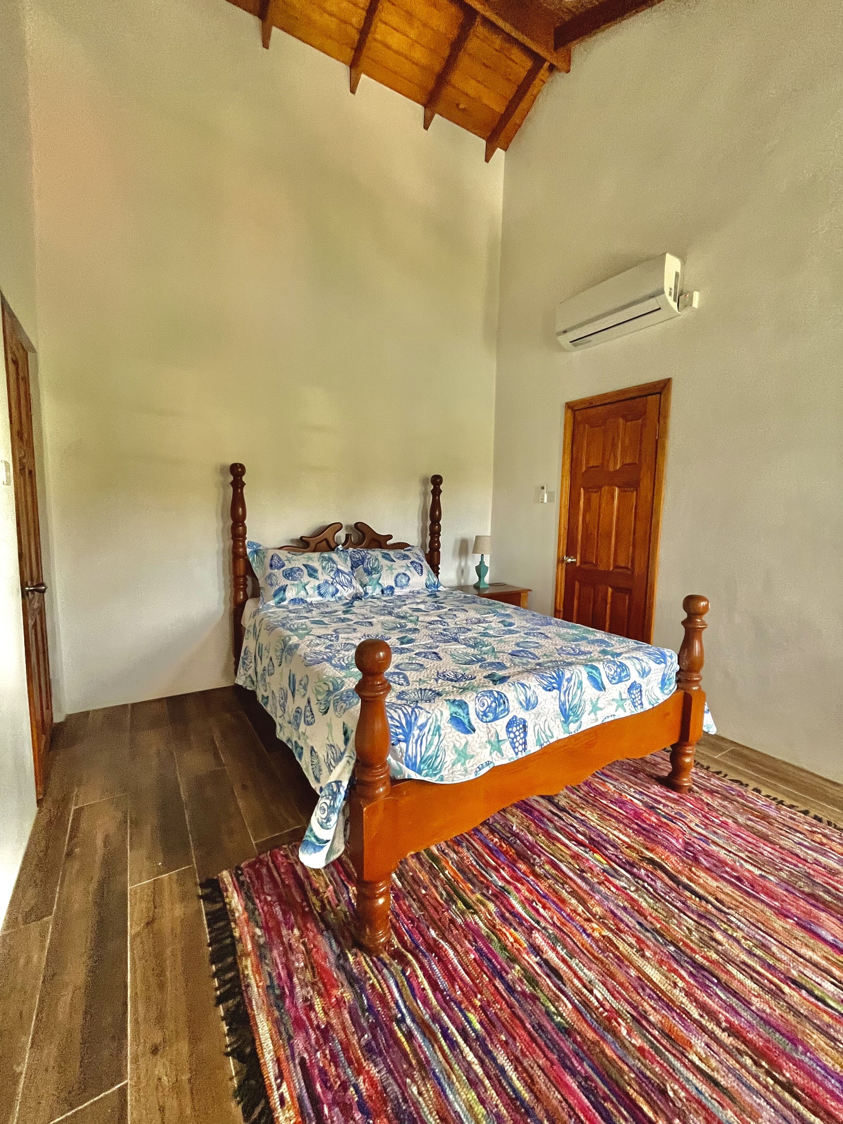 A bedroom with a wooden bed, a colorful rug, a wooden door, and a ceiling fan.