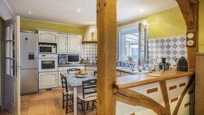 Une cuisine avec des meubles blancs, une table à manger avec des chaises, une arche en bois et une fenêtre donnant sur un beau paysage.