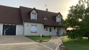 Une maison à deux étages avec une allée menant au garage, un petit jardin et un arbre sur la droite.