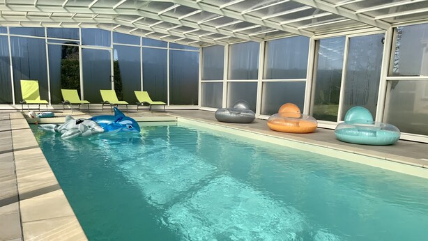 Une piscine intérieure à l’eau claire, entourée de chaises longues et de bouées gonflables.